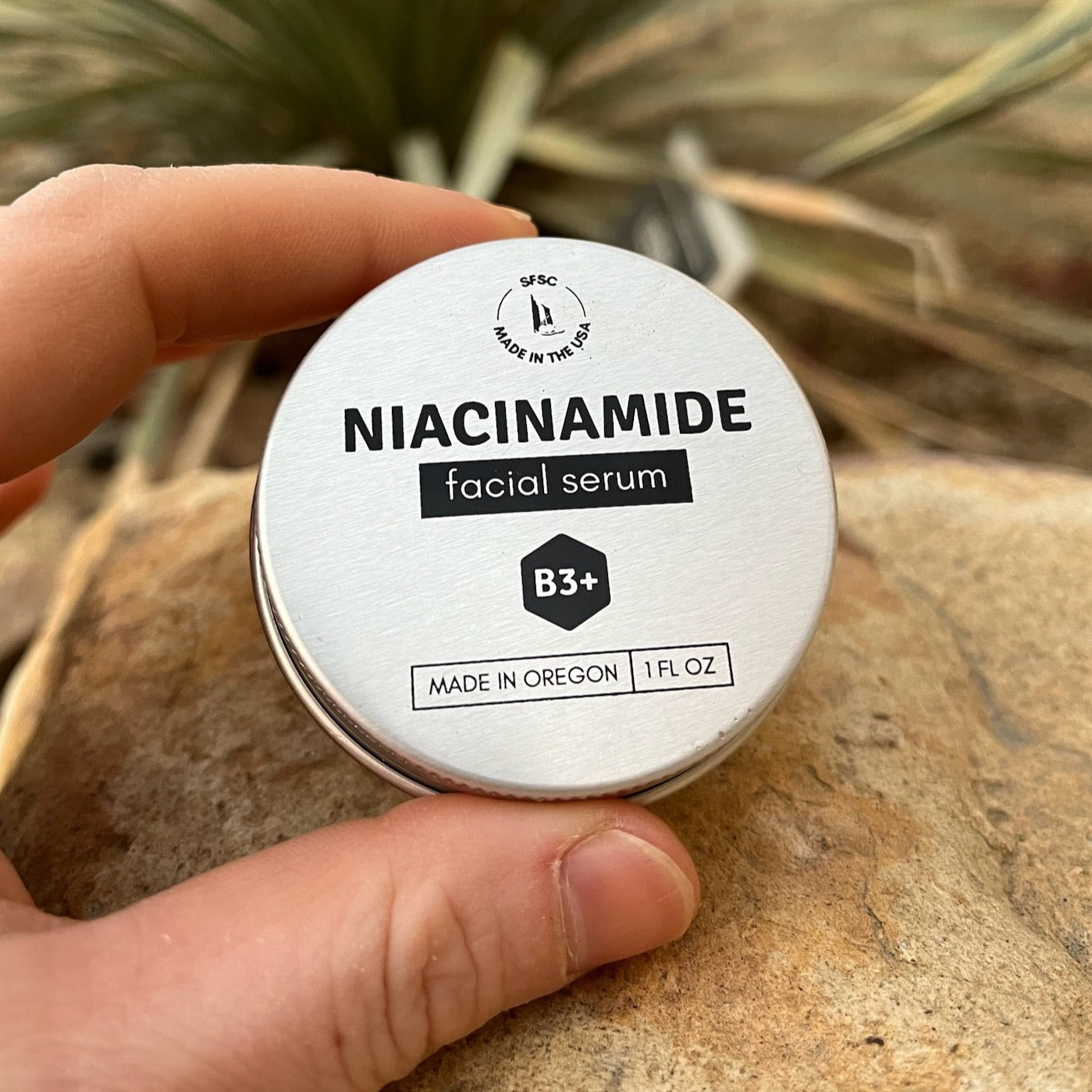 Hand holding a tin of niacinamide facial serum with a natural background
